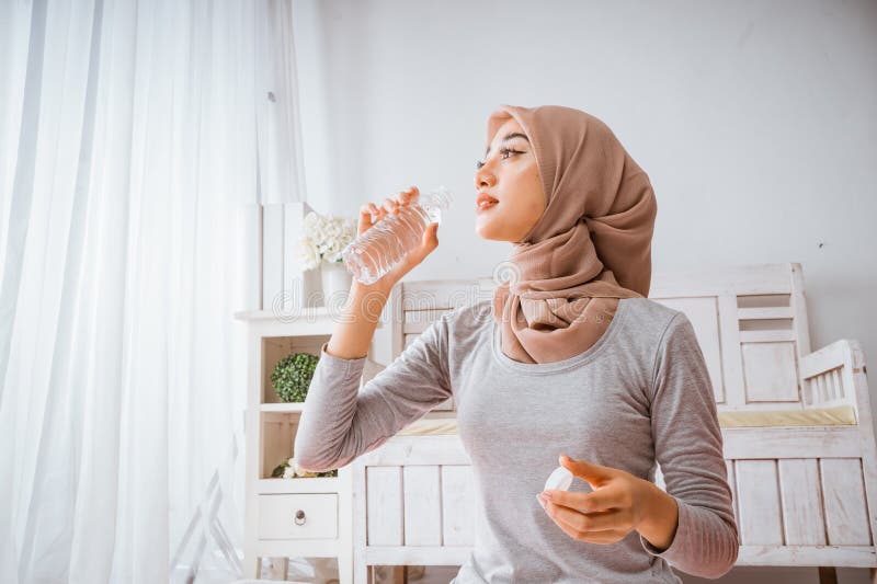 Mujer musulmana hijab sonríe bebiendo de una botella después de hacer ejercicio en casa de yoga imagen de archivo libre de regalías