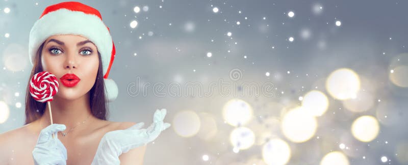 Mujer navideña. modelo de belleza niña en santa claus hat con caramelos xmas lollipop apuntando con la mano proponiendo producto fotos de archivo