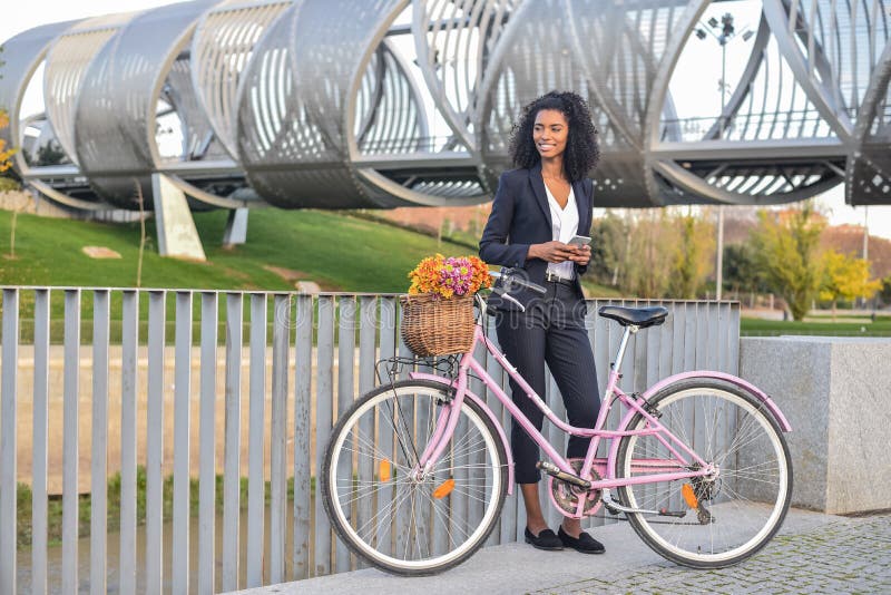 Mujer negra del negocio que hace una pausa su bicicleta del vintage que habla encendido imagen de archivo Mujer negra del negocio que hace una pausa su bicicleta del vintage que habla encendido imagen de archivo