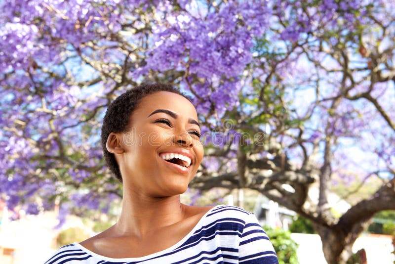 Mujer negra joven atractiva que ríe al aire libre por el árbol de la flor fotos de archivo