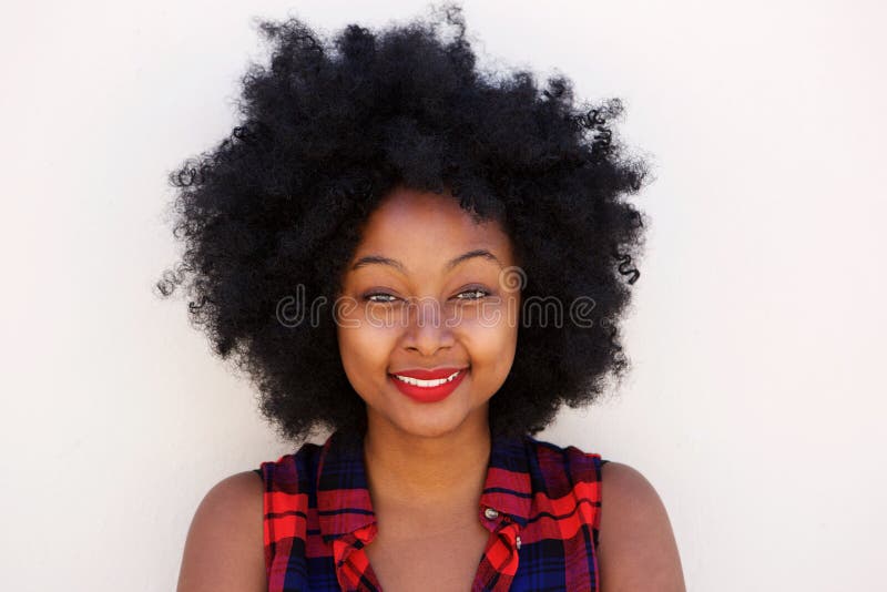 Mujer negra joven feliz con el peinado afro por la pared blanca