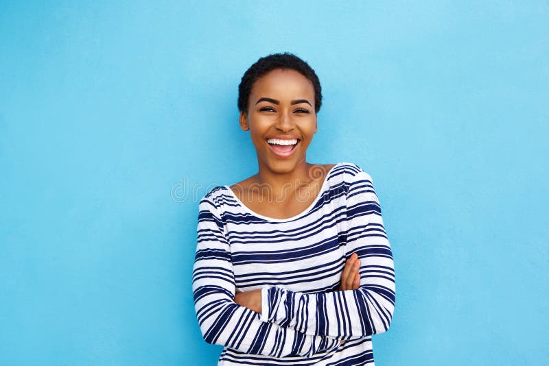 Mujer negra joven feliz que ríe contra la pared azul imagen de archivo libre de regalías