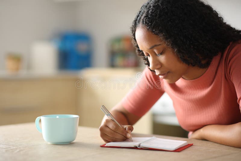Mujer negra seria tomando notas en la agenda de papel imagen de archivo