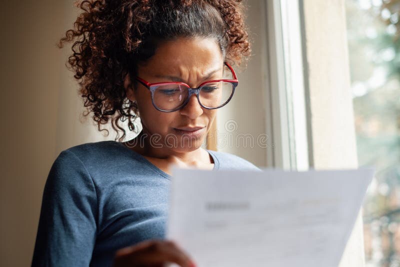 Mujer negra triste cerca de la ventana que lee el mún hoja informativa fotografía de archivo
