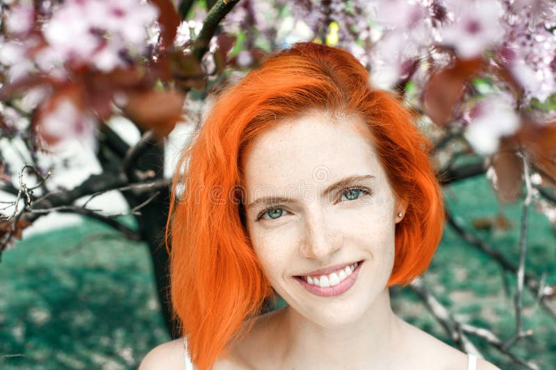 Mujer pelirroja atractiva feliz con las pecas que se colocan al aire libre en flor de cerezo de la primavera imagen de archivo libre de regalías Mujer pelirroja atractiva feliz con las pecas que se colocan al aire libre en flor de cerezo de la primavera imagen de archivo libre de regalías