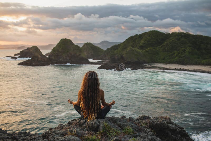 Mujer practicando yoga en loto posando al atardecer con hermosas vistas al océano fotos de archivo Mujer practicando yoga en loto posando al atardecer con hermosas vistas al océano fotos de archivo