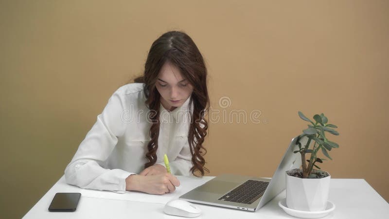 Mujer profesional enfocada escribiendo notas en la oficina con portátil y planta metrajes