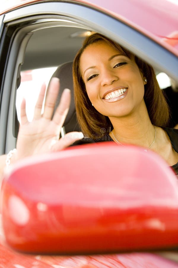 Portrait of smiling multi racial woman waving out of drivers window of vehicle, wing mirror in foreground. Portrait of smiling multi racial woman waving out of drivers window of vehicle, wing mirror in foreground.