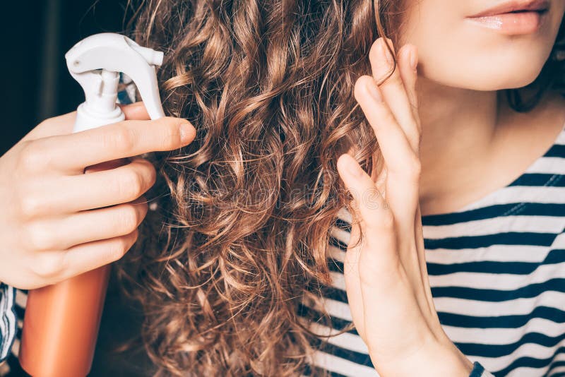 Mujer aplicando spray en cabello castaño rizado imagen de archivo