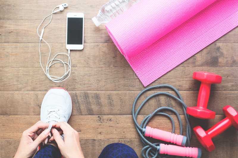 Mujer que ata encima de los zapatos del deporte, directamente arriba con equipos de deporte en piso de madera imagen de archivo Mujer que ata encima de los zapatos del deporte, directamente arriba con equipos de deporte en piso de madera imagen de archivo