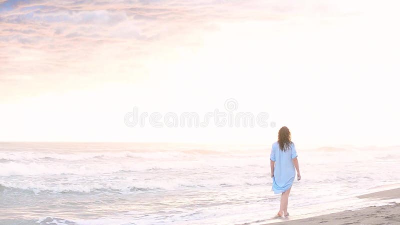 Mujer que camina a lo largo de la playa de la puesta del sol