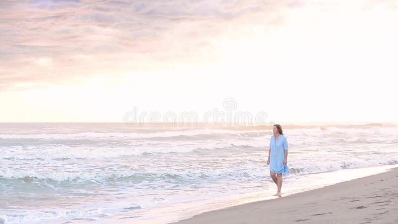 Mujer que camina a lo largo de la playa de la puesta del sol
