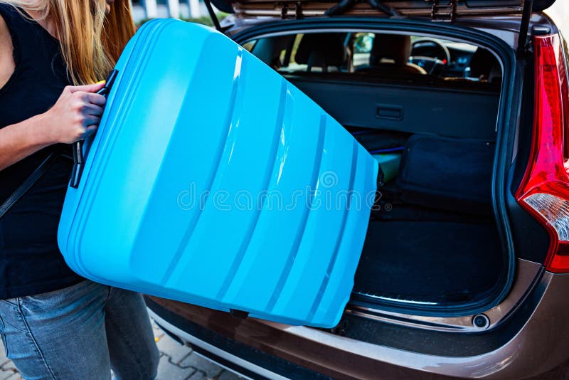 Mujer que carga dos maletas plásticas azules al tronco de coche fotografía de archivo Mujer que carga dos maletas plásticas azules al tronco de coche fotografía de archivo