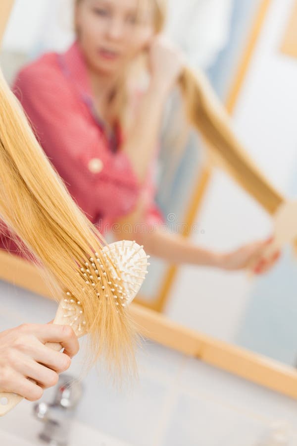 Young woman combing brushing her long blonde smooth hair in bathroom, using brush, looking in mirror. Girl taking care refreshing her hairstyle. Haircare concept. Young woman combing brushing her long blonde smooth hair in bathroom, using brush, looking in mirror. Girl taking care refreshing her hairstyle. Haircare concept.