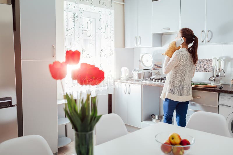 Mujer que cocina la cena en nueva cocina y que habla en el teléfono Diseño moderno de la cocina fotos de archivo libres de regalías Mujer que cocina la cena en nueva cocina y que habla en el teléfono Diseño moderno de la cocina fotos de archivo libres de regalías