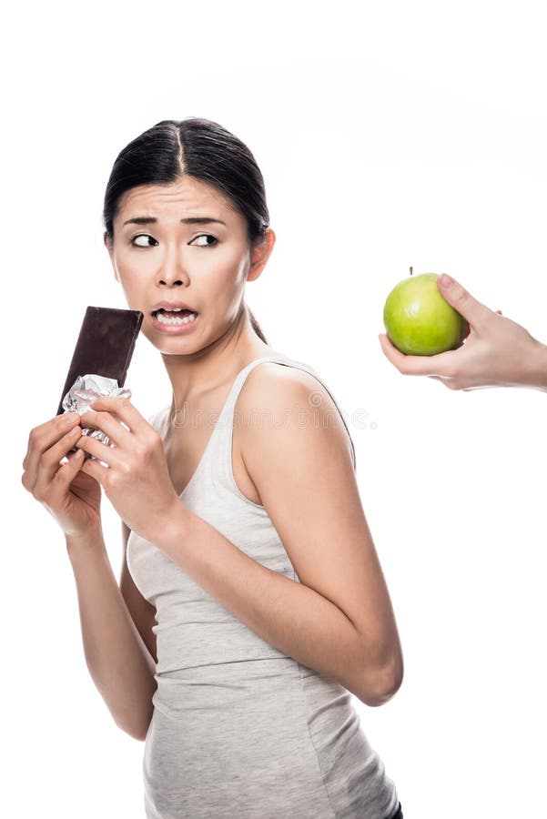 Mujer que come una manzana fresca mientras que mira el chocolate imágenes de archivo libres de regalías Mujer que come una manzana fresca mientras que mira el chocolate imágenes de archivo libres de regalías