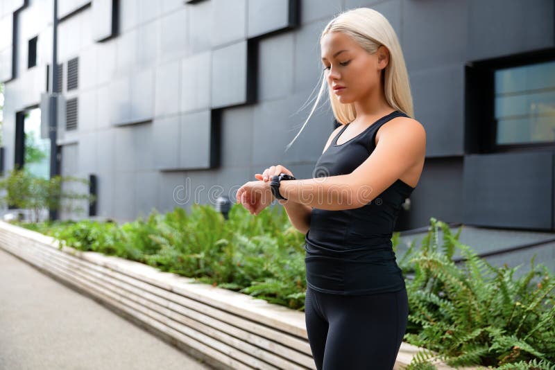 Mujer que comprueba su dispositivo elegante del reloj de la aptitud en el ambiente urbano foto de archivo Mujer que comprueba su dispositivo elegante del reloj de la aptitud en el ambiente urbano foto de archivo