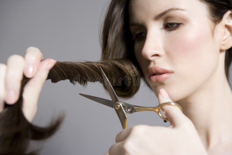 Closeup of a beautiful young woman cutting her long hair against gray background. Closeup of a beautiful young woman cutting her long hair against gray background