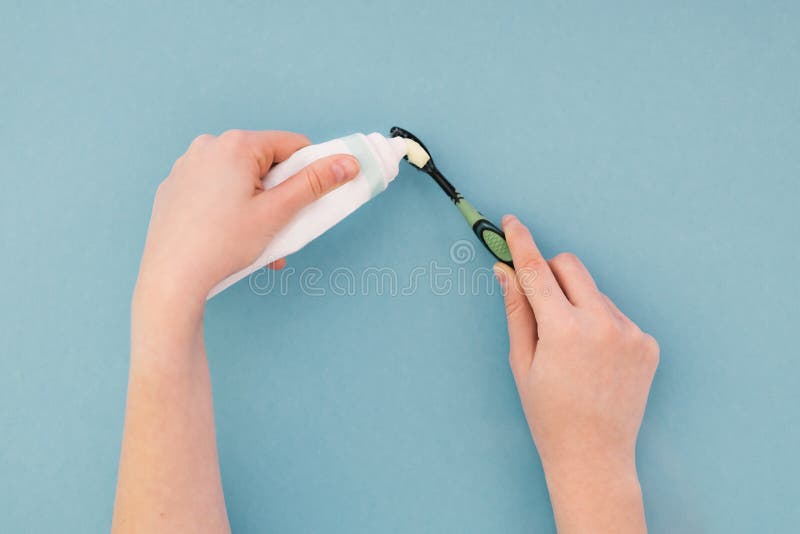 Mujer que exprime una crema dental en su cepillo de dientes con las manos en un fondo azul fotografía de archivo Mujer que exprime una crema dental en su cepillo de dientes con las manos en un fondo azul fotografía de archivo
