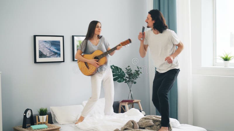 Mujer que juega al individuo de la guitarra que canta en teledirigido y que baila en cama en casa