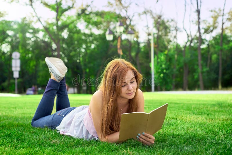 Mujer que miente en un césped con un diario imagenes de archivo Mujer que miente en un césped con un diario imagenes de archivo