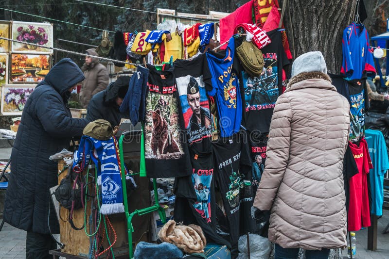Mujer que mira las camisetas con Vladimir Putin en un pequeño mercado fotografía de archivo libre de regalías Mujer que mira las camisetas con Vladimir Putin en un pequeño mercado fotografía de archivo libre de regalías