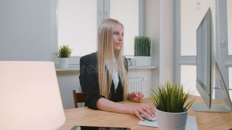 Mujer que muestra los pulgares abajo en oficina El sentarse en la hembra rubia joven del lugar de trabajo en el traje de negocios