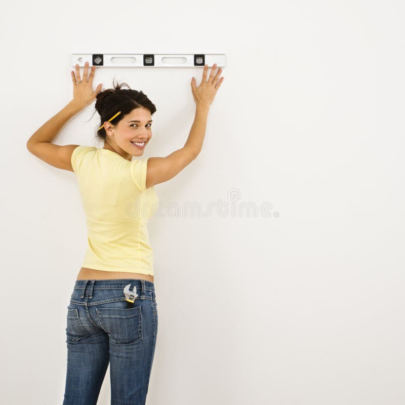 Woman standing holding level up to interior wall and smiling. Woman standing holding level up to interior wall and smiling.