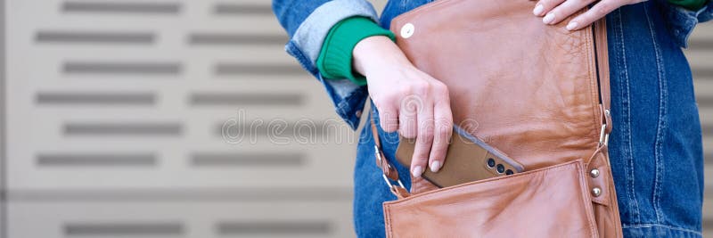 Woman putting mobile phone in brown leather handbag closeup. Storage and organization concept. Woman putting mobile phone in brown leather handbag closeup. Storage and organization concept