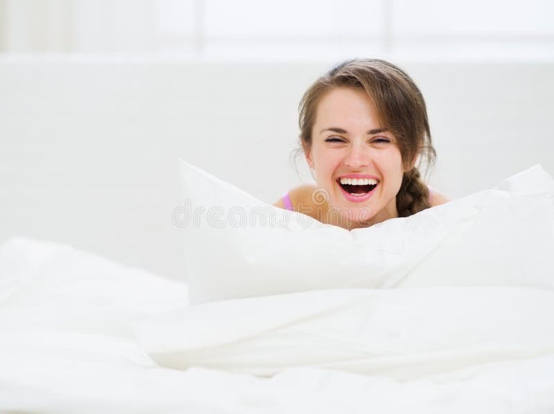 Smiling woman laying in bed and hiding behind pillow. Smiling woman laying in bed and hiding behind pillow