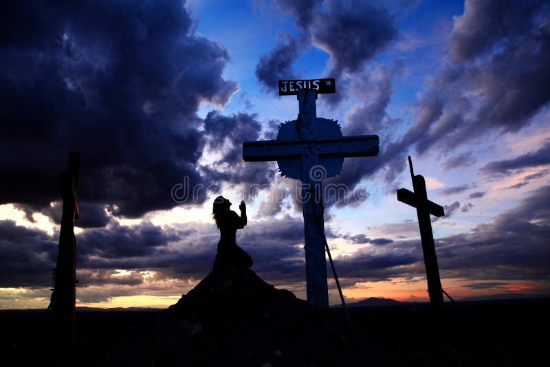 Mujer que ruega en la cruz en puesta del sol