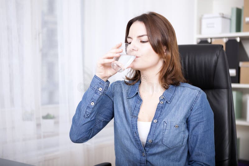 Mujer que se sienta en el agua potable de la silla de la oficina imágenes de archivo libres de regalías Mujer que se sienta en el agua potable de la silla de la oficina imágenes de archivo libres de regalías