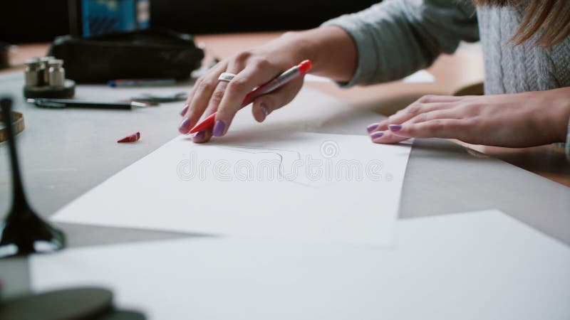 Mujer que se sienta en la tabla en oficina, sosteniendo el lápiz y dibujando el bosquejo de zapatos en el papel Resbalador derech