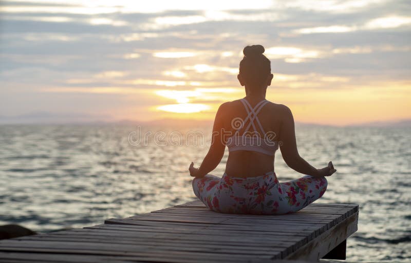 Mujer que se sienta en la yoga que medita actitud en el lado de mar contra beauti foto de archivo libre de regalías Mujer que se sienta en la yoga que medita actitud en el lado de mar contra beauti foto de archivo libre de regalías