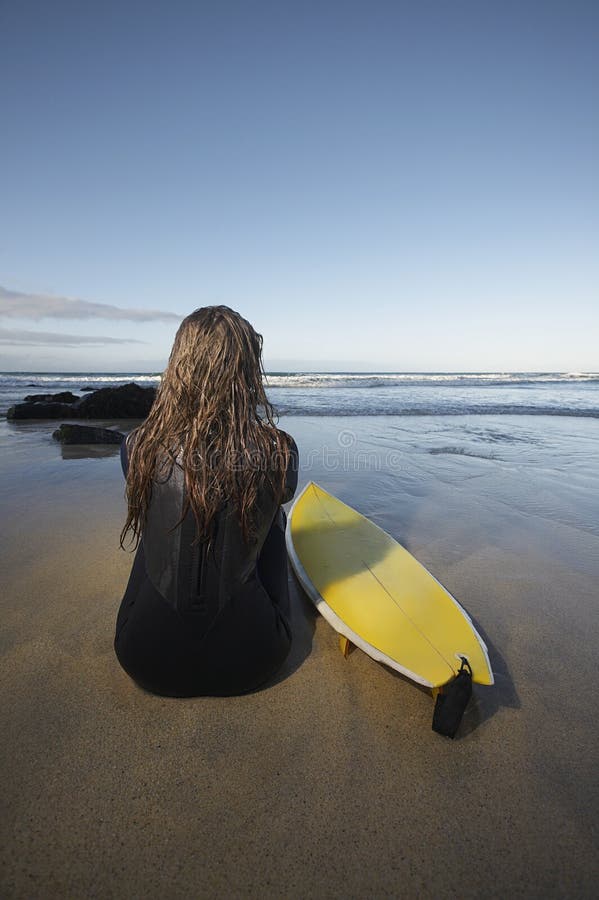 Mujer que se sienta por la tabla hawaiana en la playa fotografía de archivo libre de regalías Mujer que se sienta por la tabla hawaiana en la playa fotografía de archivo libre de regalías