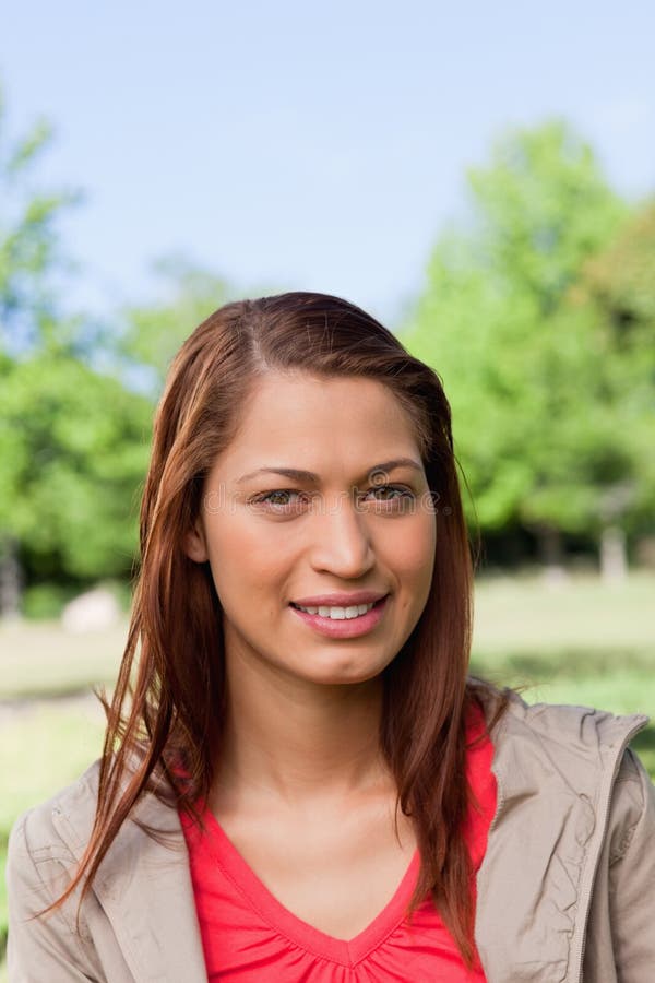 Mujer que sonríe como ella mira derecho delante de ella en un parque fotografía de archivo libre de regalías Mujer que sonríe como ella mira derecho delante de ella en un parque fotografía de archivo libre de regalías