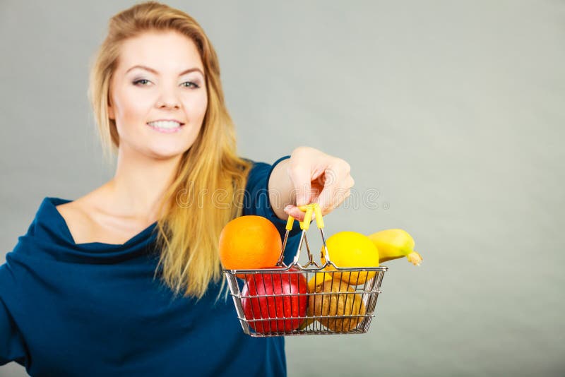 Mujer que sostiene la cesta de compras con las frutas dentro. Comida sana de compra, vegetariano, gluten libremente, productos del vegano Mujer que sostiene el carro de la compra con las frutas dentro