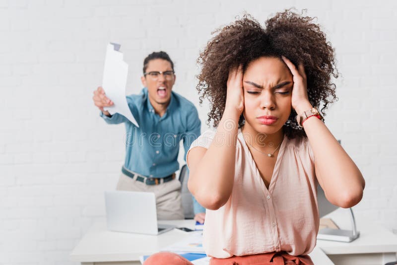 Mujer que sufre de la tensión debido a colega masculino enojado imagen de archivo Mujer que sufre de la tensión debido a colega masculino enojado imagen de archivo