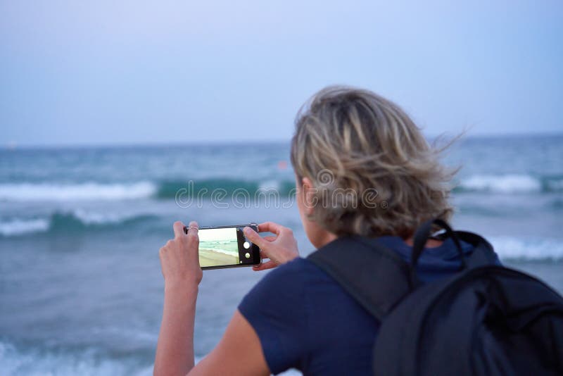 Mujer que toma una foto de un mar en el tel? fono elegante en puesta del sol fotos de archivo libres de regalías