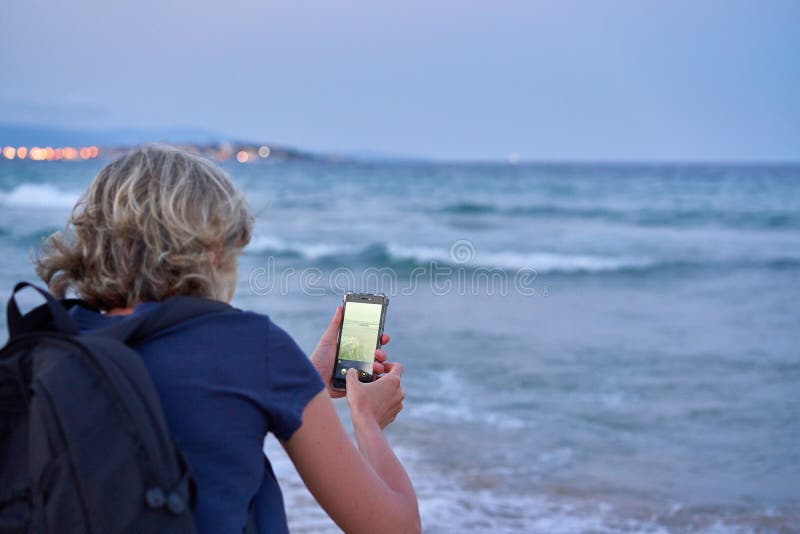 Mujer que toma una foto de un mar en el tel? fono elegante en puesta del sol fotografía de archivo