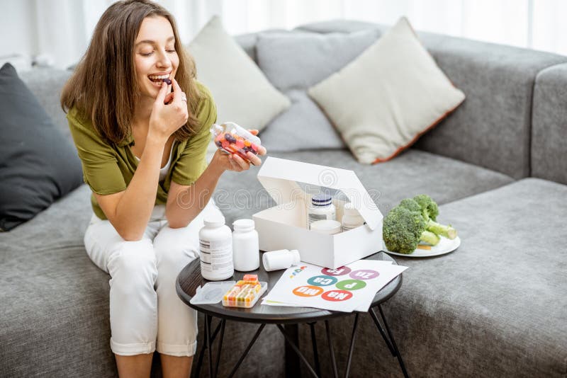 Woman taking vitamins or nutritional supplements in the form of pills while sitting on the couch at home. Concept of biohacking and preventive medicine. Woman taking vitamins or nutritional supplements in the form of pills while sitting on the couch at home. Concept of biohacking and preventive medicine