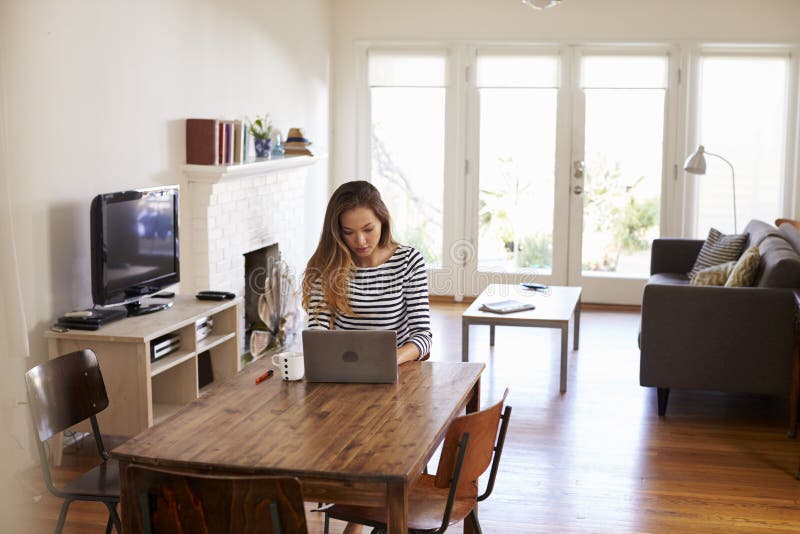 Mujer que trabaja de hogar usando el ordenador portátil en la mesa de comedor imagen de archivo libre de regalías
