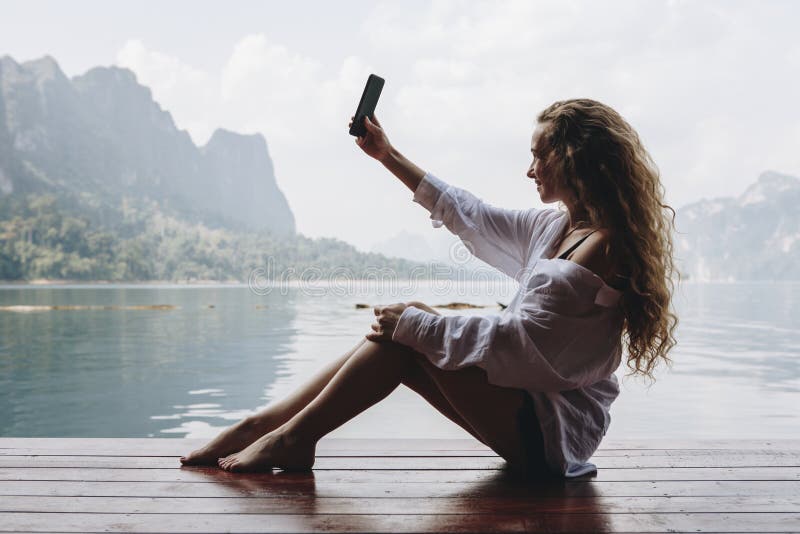 Mujer que usa su teléfono por un lago imagen de archivo Mujer que usa su teléfono por un lago imagen de archivo