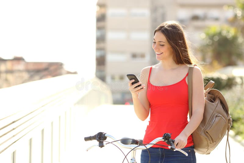 Mujer que usa un teléfono elegante que camina con una bicicleta Mujer que usa un teléfono elegante que camina con una bicicleta