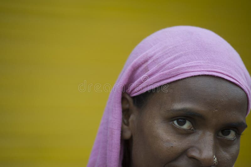 Pushkar, Rajasthan, India - August 06, 2011: Detail of Rajasthani woman´s face with dark skin and smiling eyes, wearing pink shawl, walking in front of an outdoor plain yellow background copy space. Pushkar, Rajasthan, India - August 06, 2011: Detail of Rajasthani woman´s face with dark skin and smiling eyes, wearing pink shawl, walking in front of an outdoor plain yellow background copy space