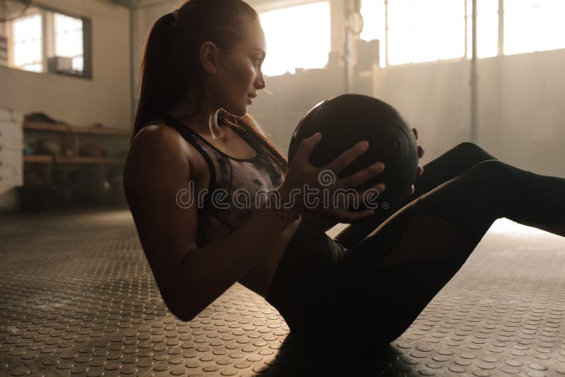 Mujer resuelta que ejercita con la bola de medicina en gimnasio
