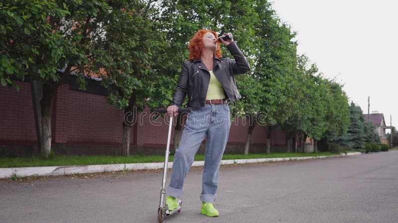 Mujer retro, segura de sí misma, de pie al aire libre con patín que bebe agua de soda en cámara lenta almacen de metraje de vídeo