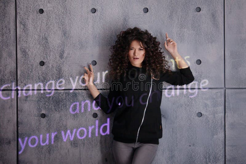 Mujer rizada posando activamente sobre un fondo de pared con luz coloreada Cambiar sus pensamientos y cambiar su mundo imagen de archivo