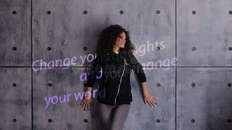 Mujer rizada posando activamente sobre un fondo de pared con luz coloreada Cambiar sus pensamientos y cambiar su mundo imagenes de archivo