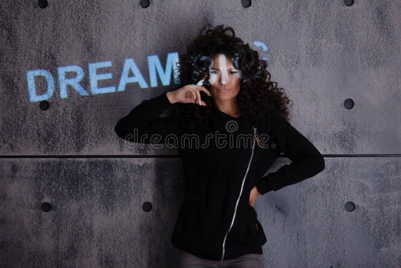 Mujer rizada posando activamente sobre un fondo de pared de concreto. En la pared se proyecta una inscripciÃ³n luminosa de color imagen de archivo libre de regalías